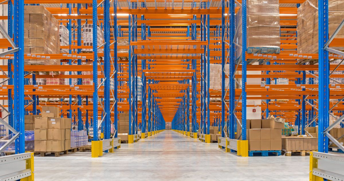 Large warehouse with tall blue and orange pallet racks, stocked with boxes and products.